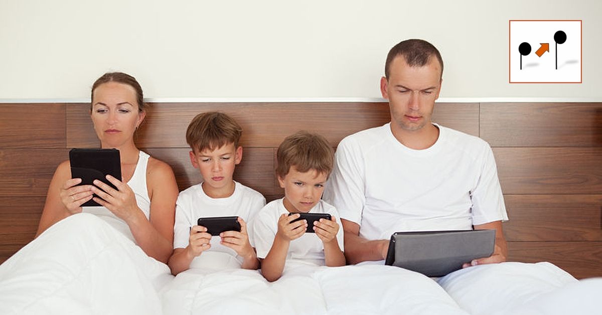 Celá rodina sedí v posteli a kouká do svých mobilů, tabletů,...
